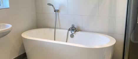 Un baño moderno con una bañera independiente, un cabezal de ducha de mano y un lavamanos empotrado.