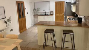 Una cocina moderna con encimeras de madera, una isla central con taburetes, armarios blancos y un reloj a la vista.