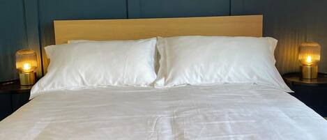 A bed with white linens, two bedside lamps, and a wooden headboard.