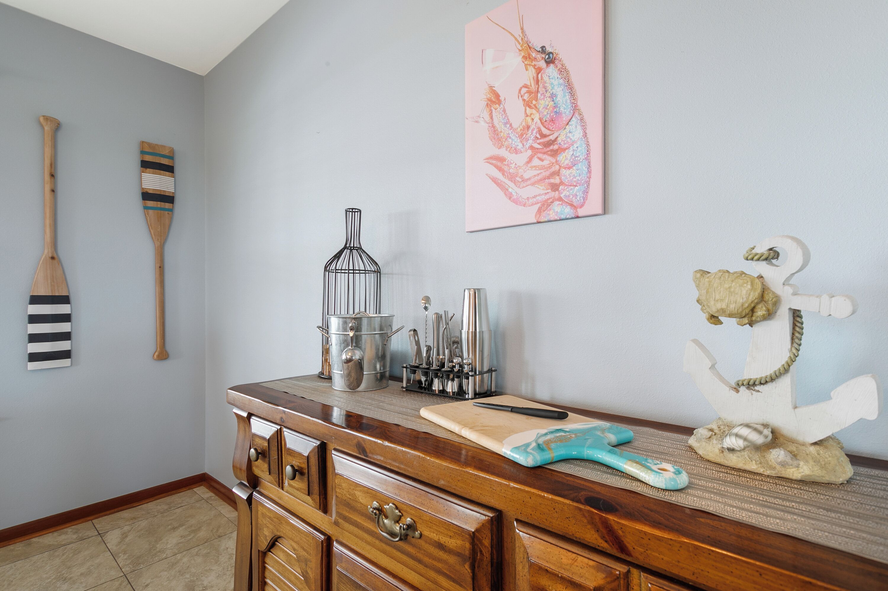 A kitchen with wooden cabinets, a cutting board, a knife, a metal pot, and a lobster painting on the wall.