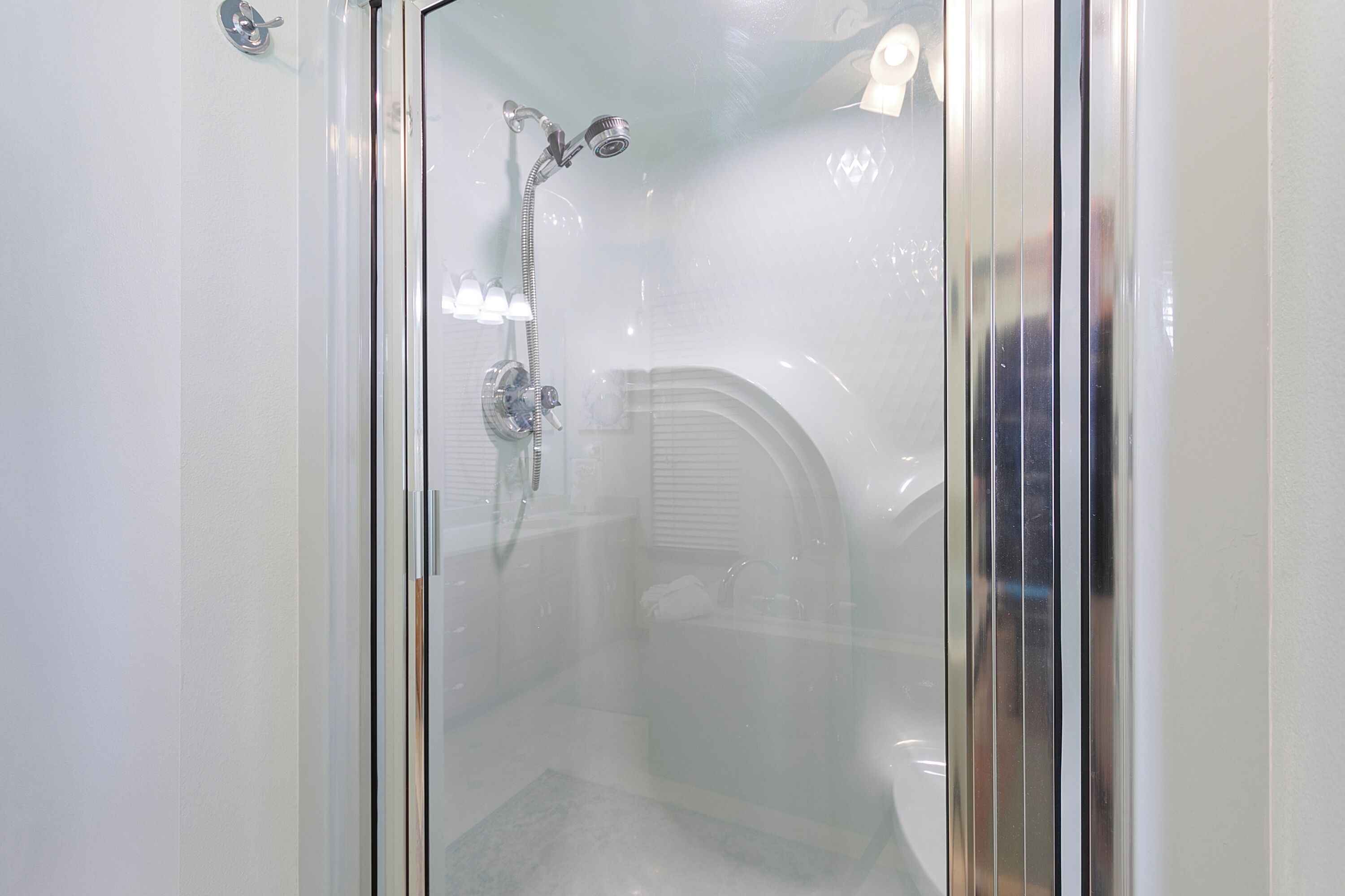 A glass-enclosed shower with a handheld showerhead and a wall-mounted faucet.