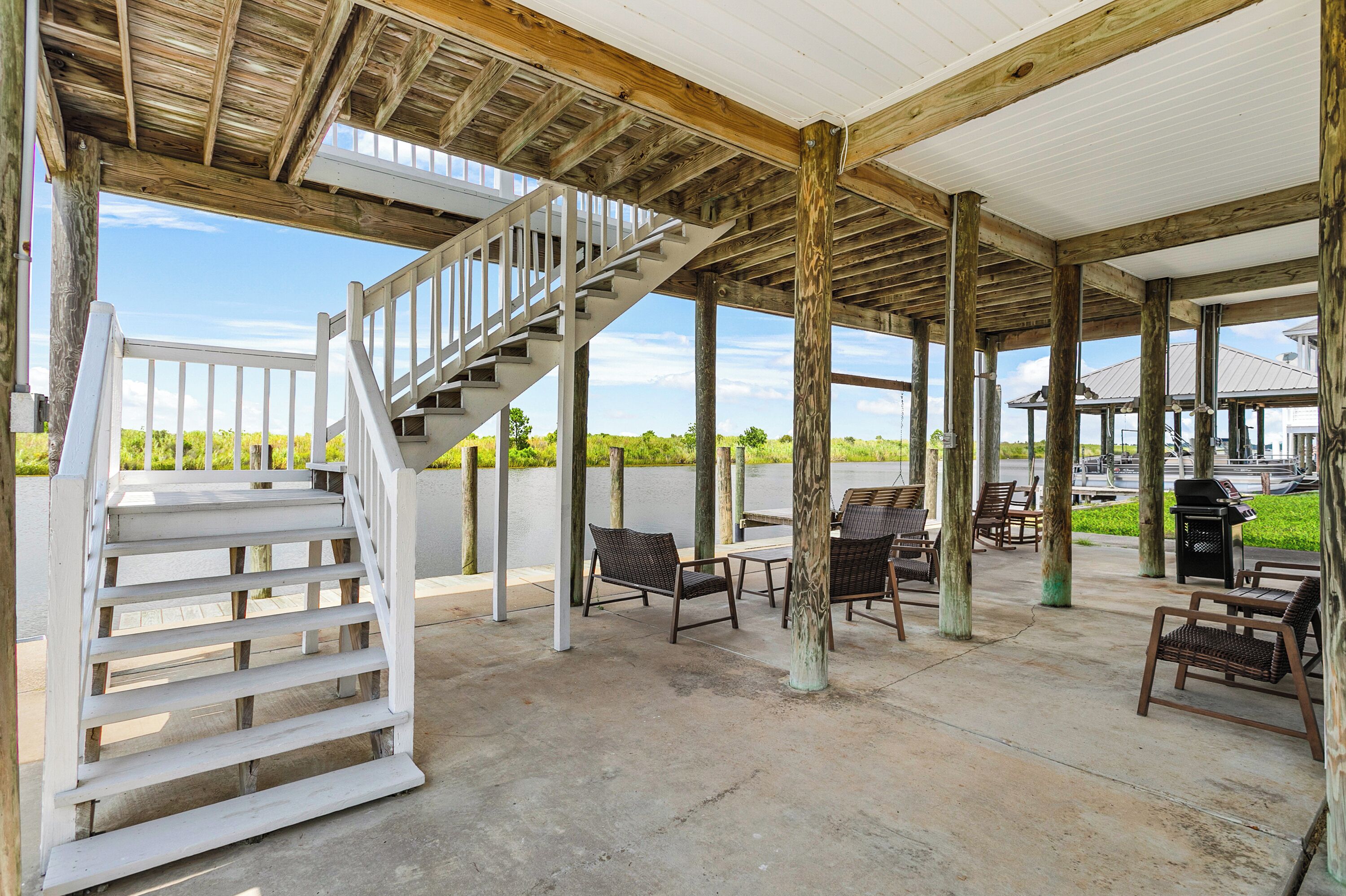 A covered outdoor area with a wooden staircase, seating, and a view of the water.