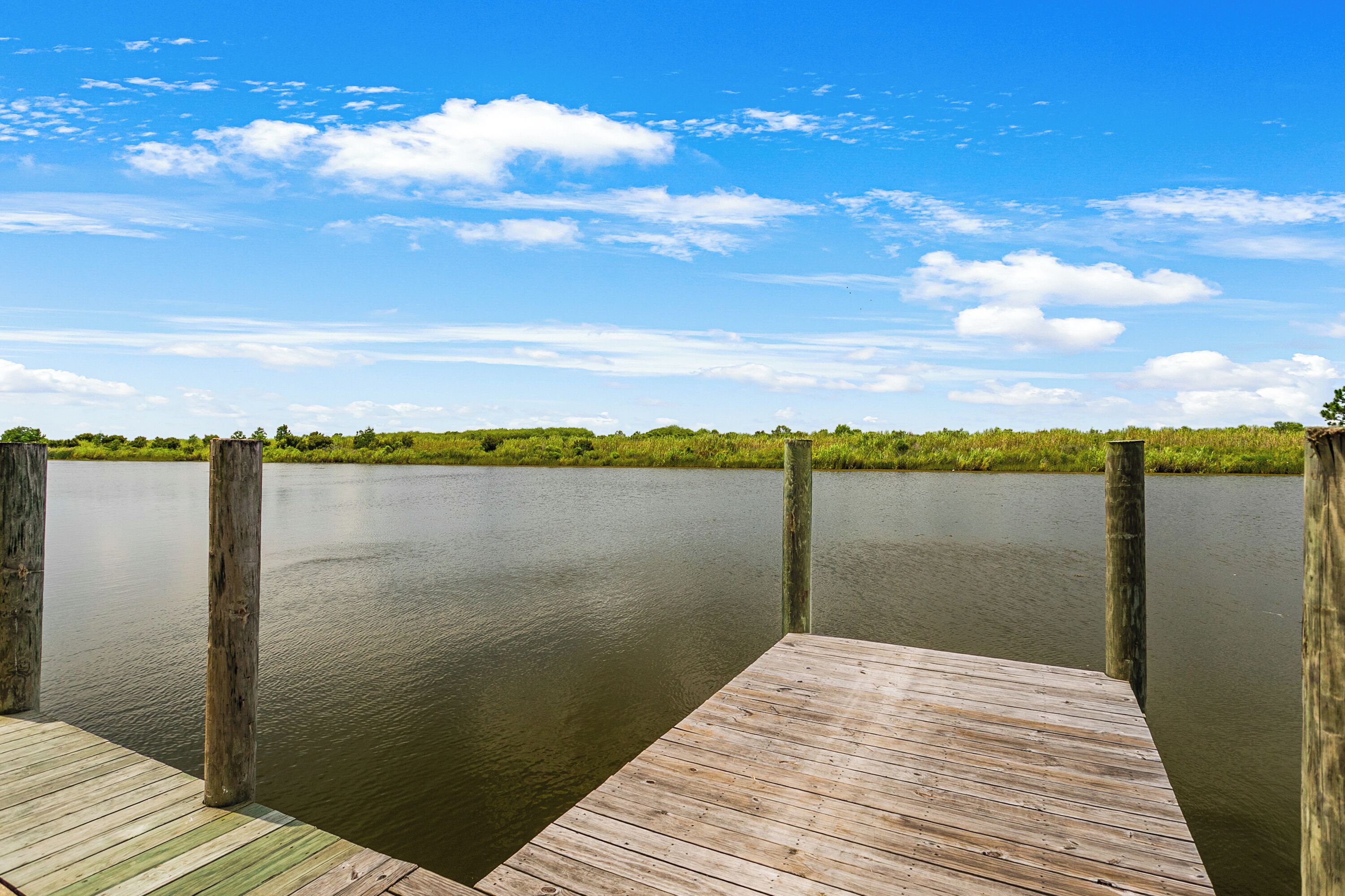 A wooden dock extending into a calm body of water with a clear sky above.