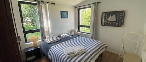 Ein Schlafzimmer mit einem Bett, zwei Fenstern, einer Lampe, einem gerahmten Bild und einer Heizung.