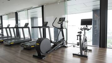 A gym with treadmills, an elliptical, and a stationary bike, large windows, and a city view.