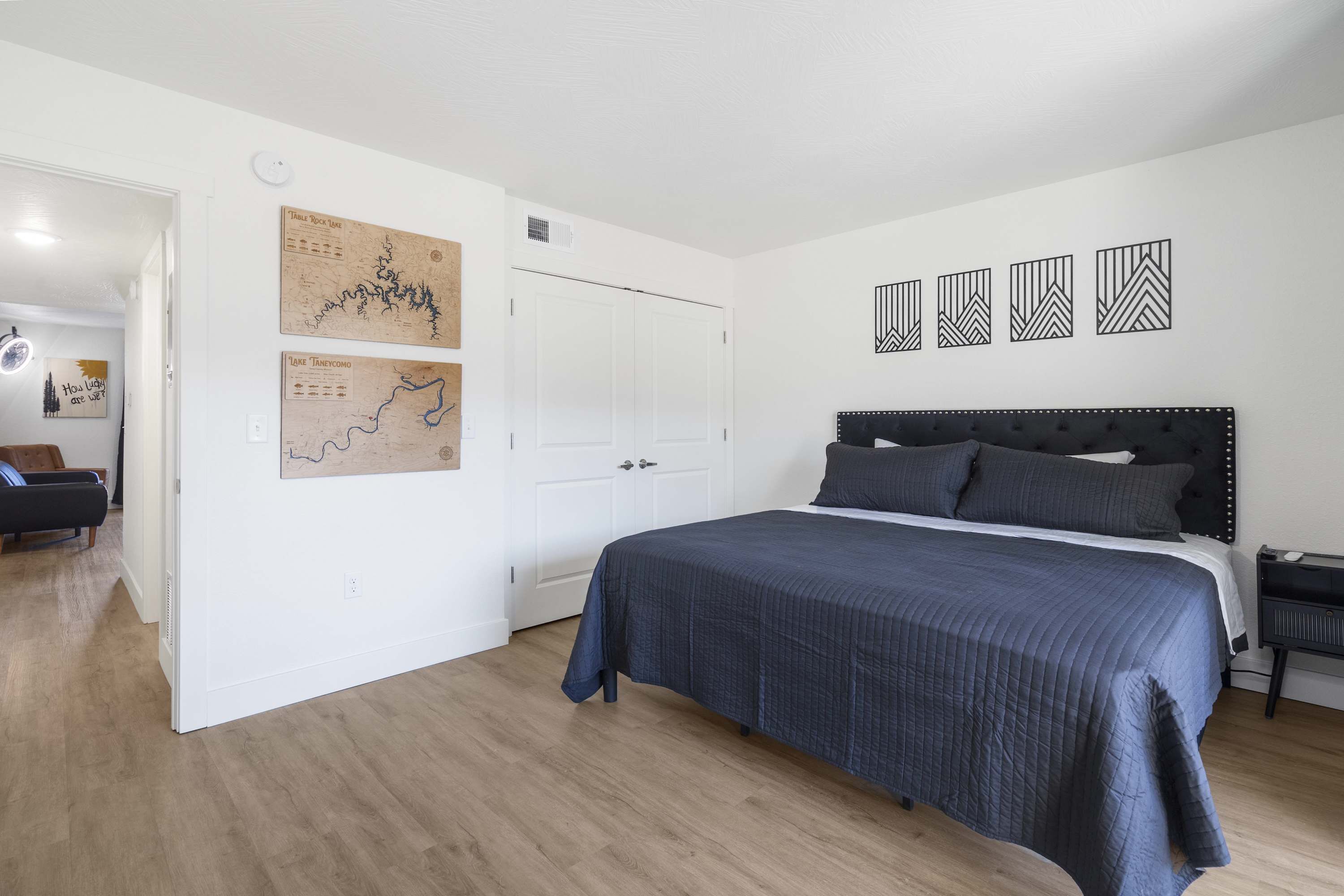 Une chambre avec un grand lit, une armoire et une porte donnant sur une autre pièce. On y trouve des œuvres d’art murales et une tête de lit ornée d’un motif.