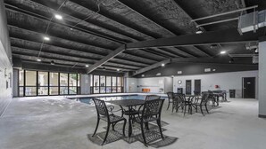 Ein Innenpoolbereich mit Betonboden, Metalltischen und -stühlen sowie einer Decke mit freiliegenden Balken.