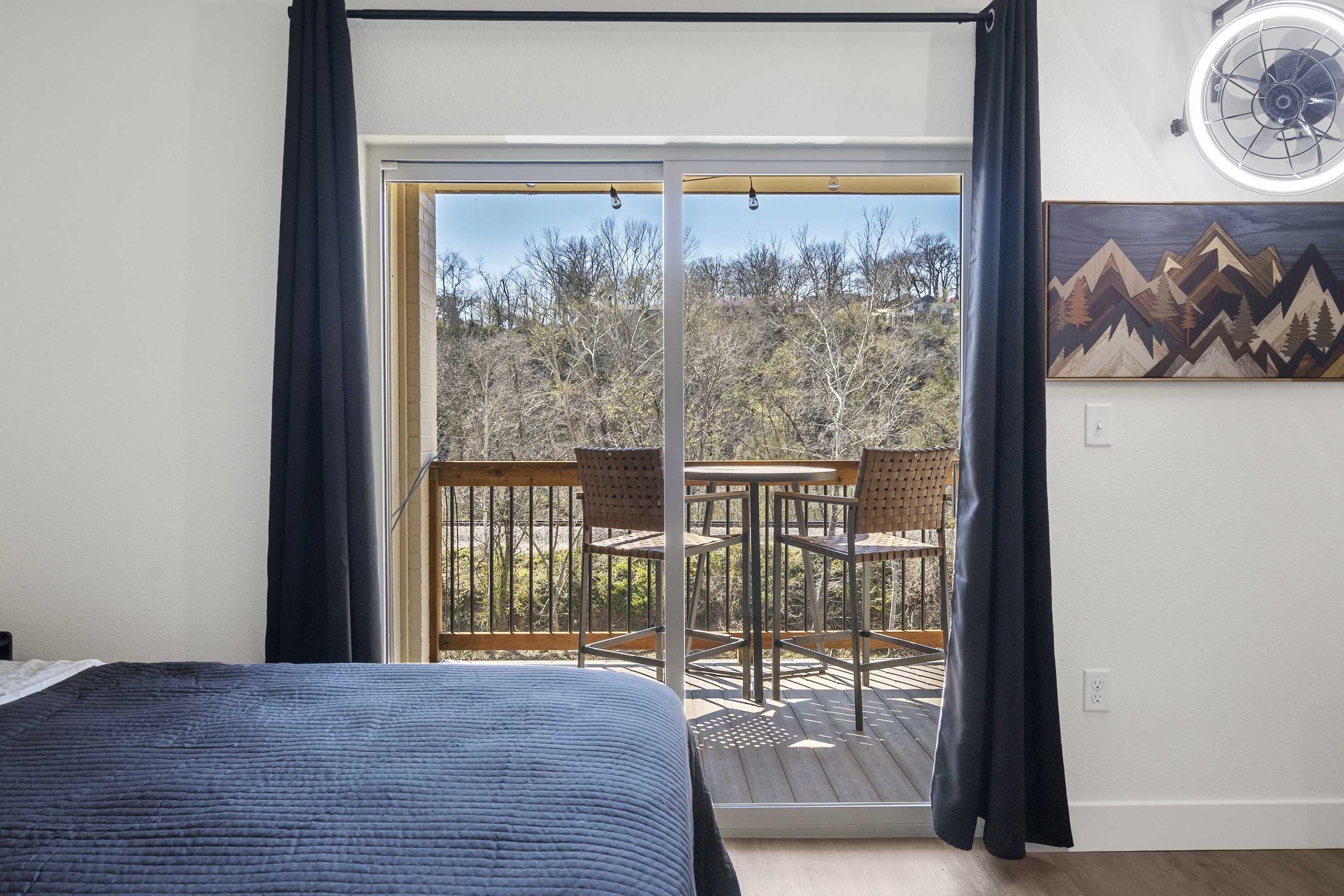 A bedroom with a bed, a balcony with a table and chairs, and a painting on the wall.