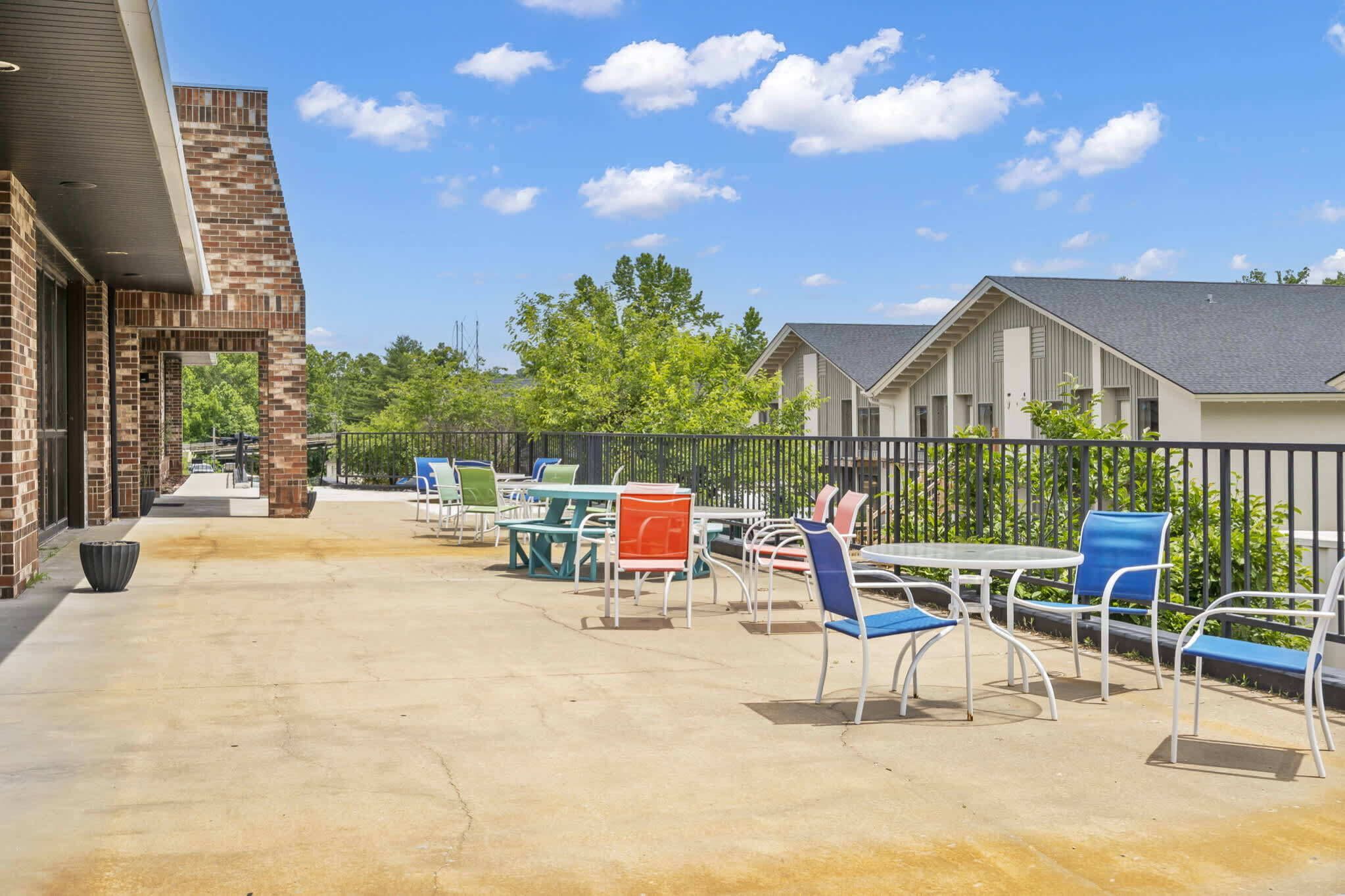 An outdoor patio area with multiple tables and chairs, a brick building, and a fence.