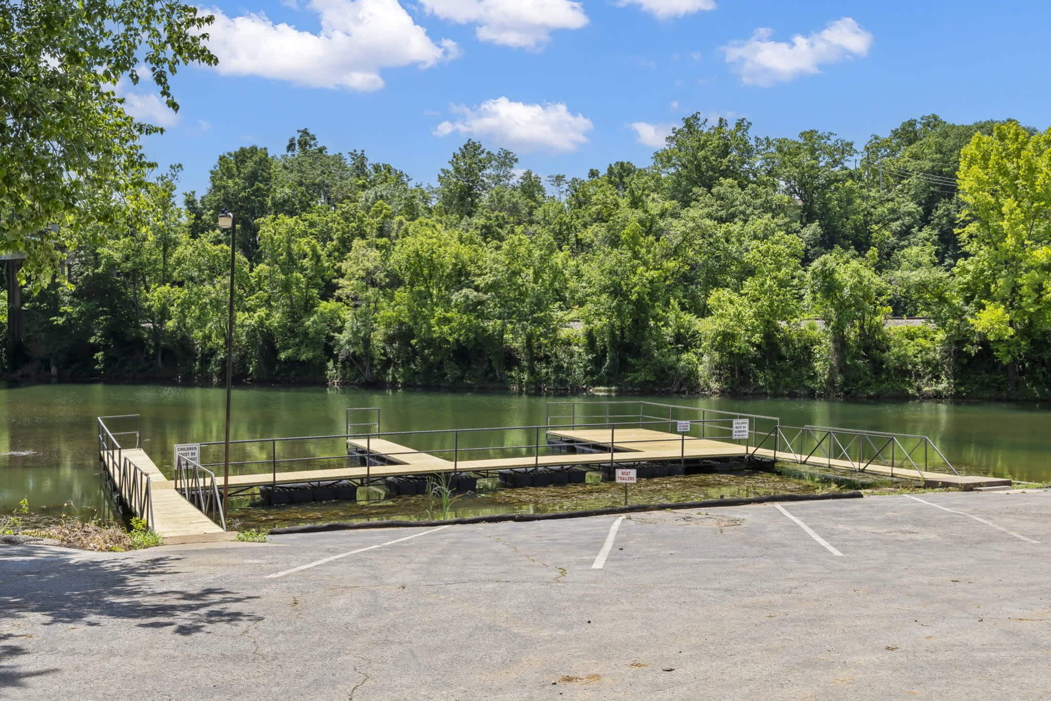 A parking area with a dock extending into a lake, surrounded by dense trees.