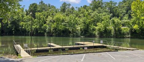 A parking area with a dock extending into a lake, surrounded by dense trees.