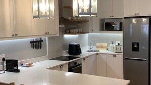 A modern kitchen with white cabinets, a central island, hanging lights, and stainless steel appliances.