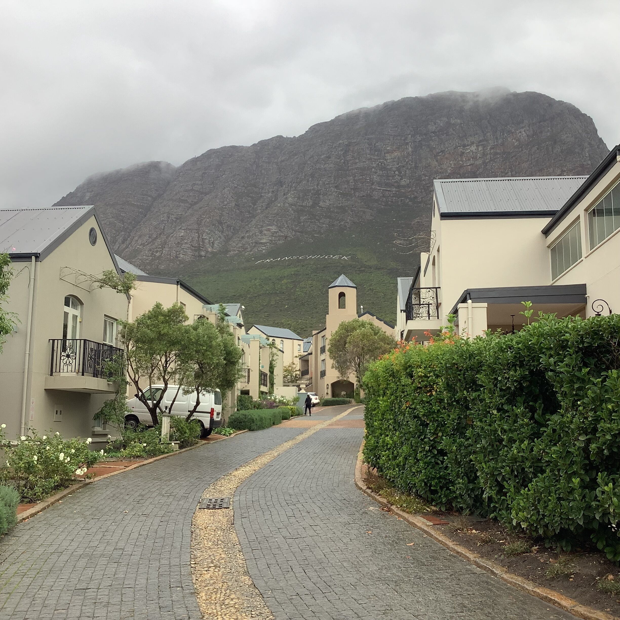 A cobblestone street lined with buildings, a church with a bell tower, and a mountain in the background.
