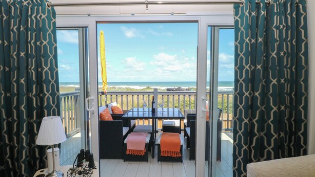 A balcony with a table and chairs, a lamp, and a view of the ocean. - Sand & Serenity (Norwich)