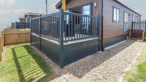 A modern, single-story cabin with a deck, surrounded by a wooden fence and gravel path. - Sand & Serenity (Norwich)