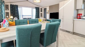 A modern dining area with teal upholstered chairs, a wooden table, and a pendant light. - Sand & Serenity (Norwich)