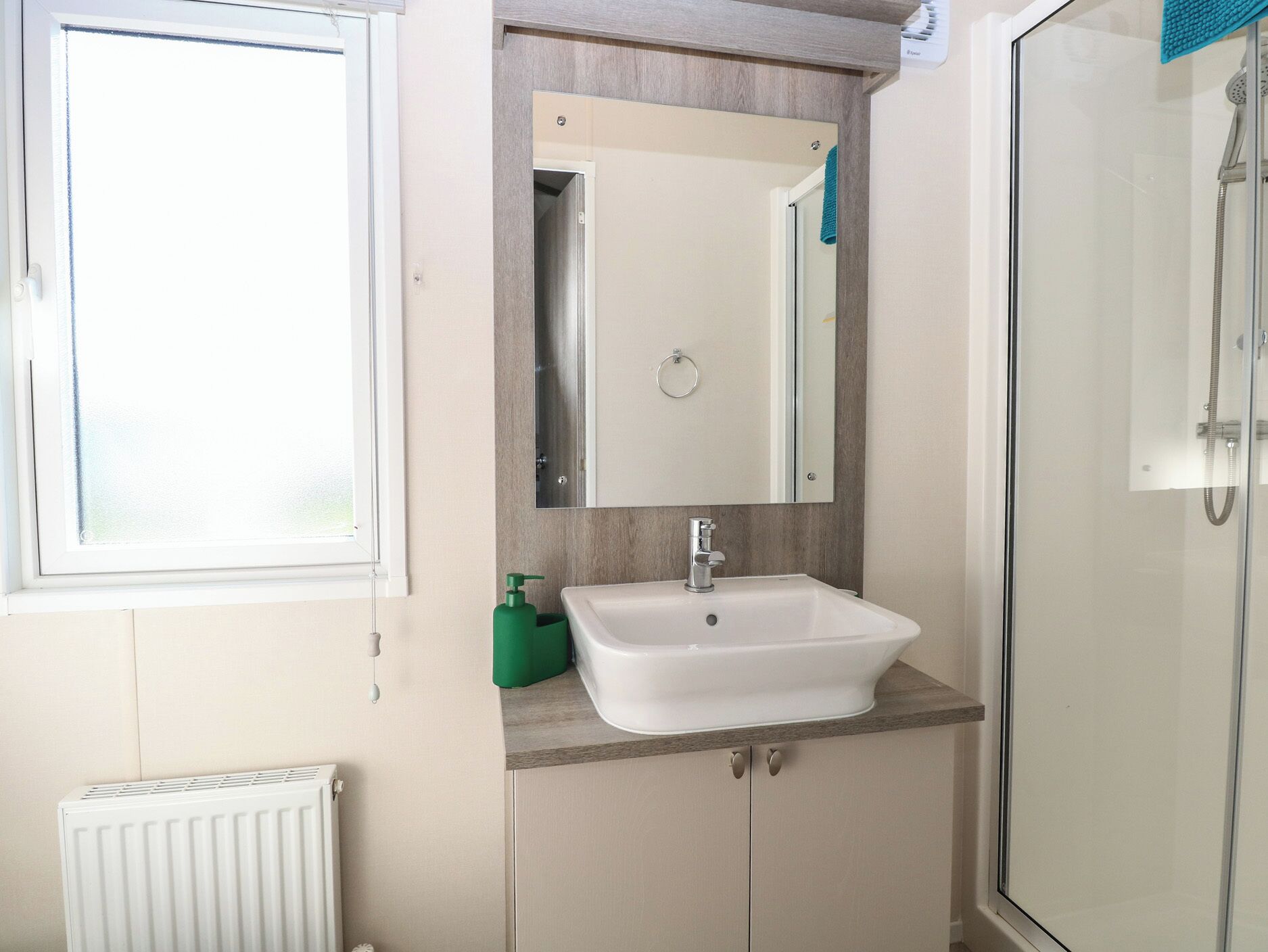 A bathroom with a white sink, a mirror above it, a towel rack, and a shower area.