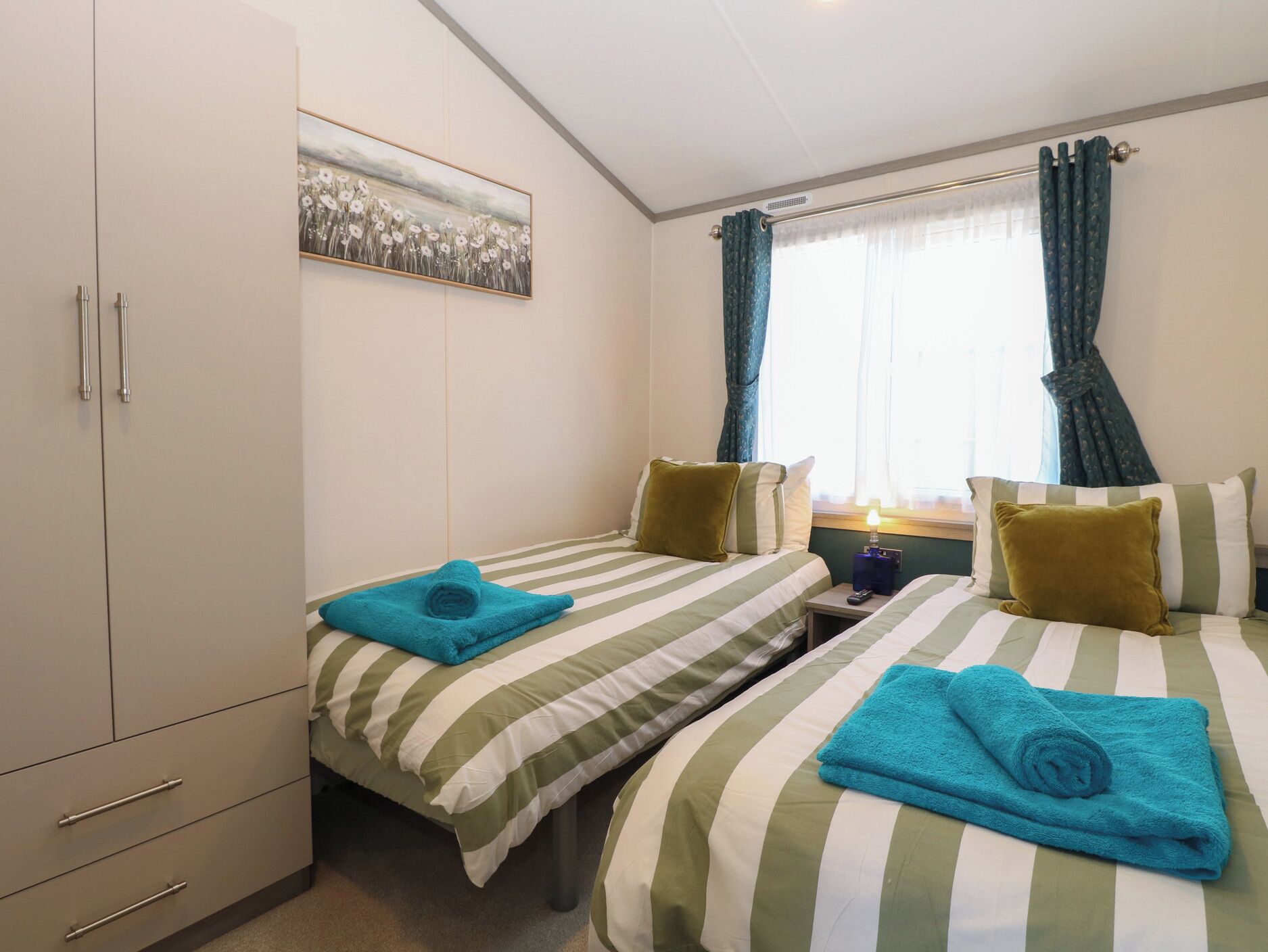 A hotel room with two beds, striped bedding, a wardrobe, a painting, and curtains.