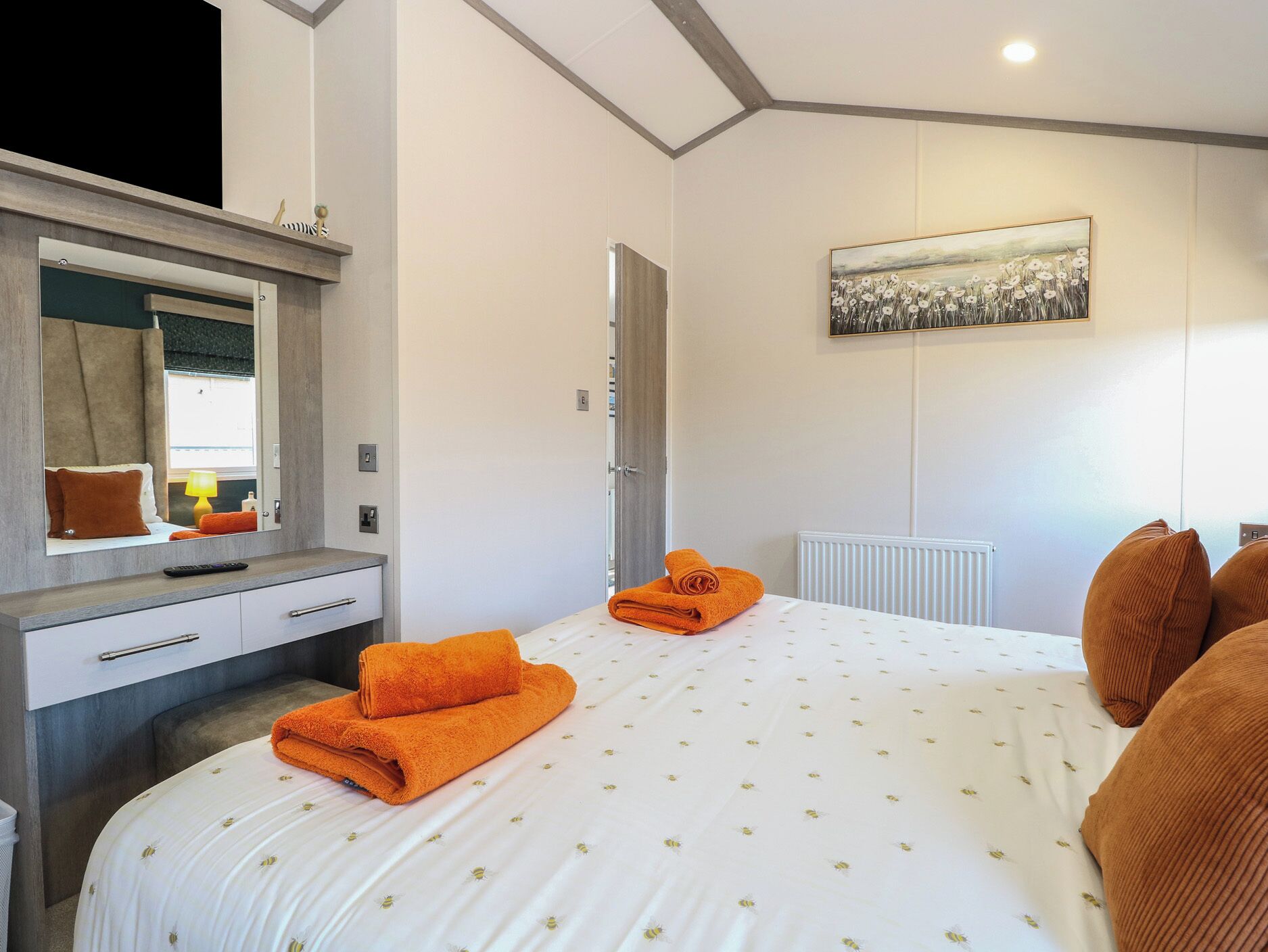 Una habitación de hotel con una cama, un espejo grande, un cuadro en la pared y un radiador.