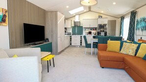 A modern living room with a flat-screen TV, a sofa, and a dining area with chairs. - Sand & Serenity (Norwich)