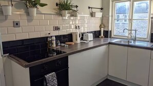 A modern kitchen with white cabinetry, a black countertop, and a window with a view of buildings. - 1840's Converted Railway Cottage (Swindon)