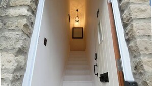 A narrow stairway with white steps leading to a landing, flanked by stone walls and a wooden door frame. - 1840's Converted Railway Cottage (Swindon)