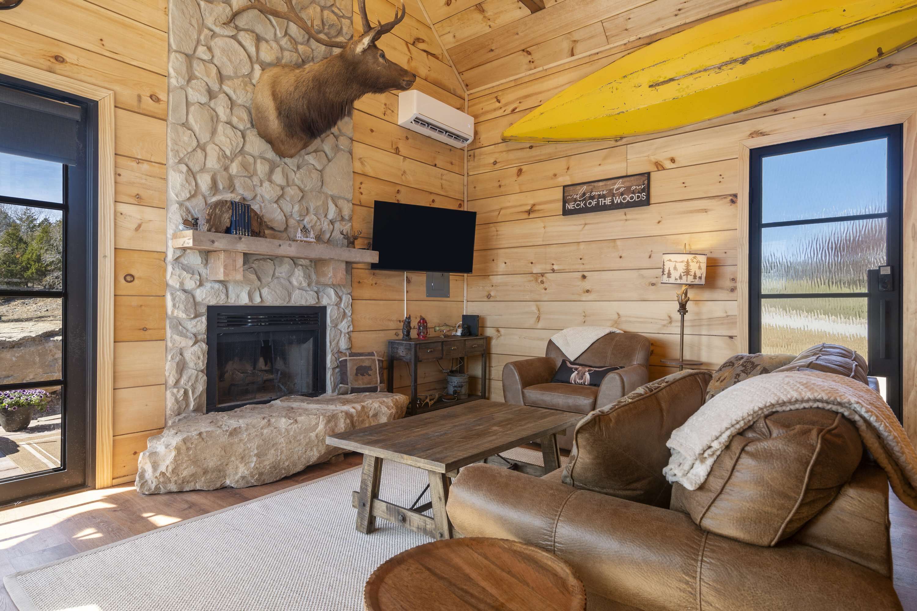 L’intérieur chaleureux d’un chalet avec une cheminée en pierre, un canapé en cuir et une tête de cerf accrochée au mur.