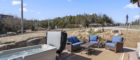 An outdoor patio area with a hot tub, wicker furniture, and a view of a natural landscape.