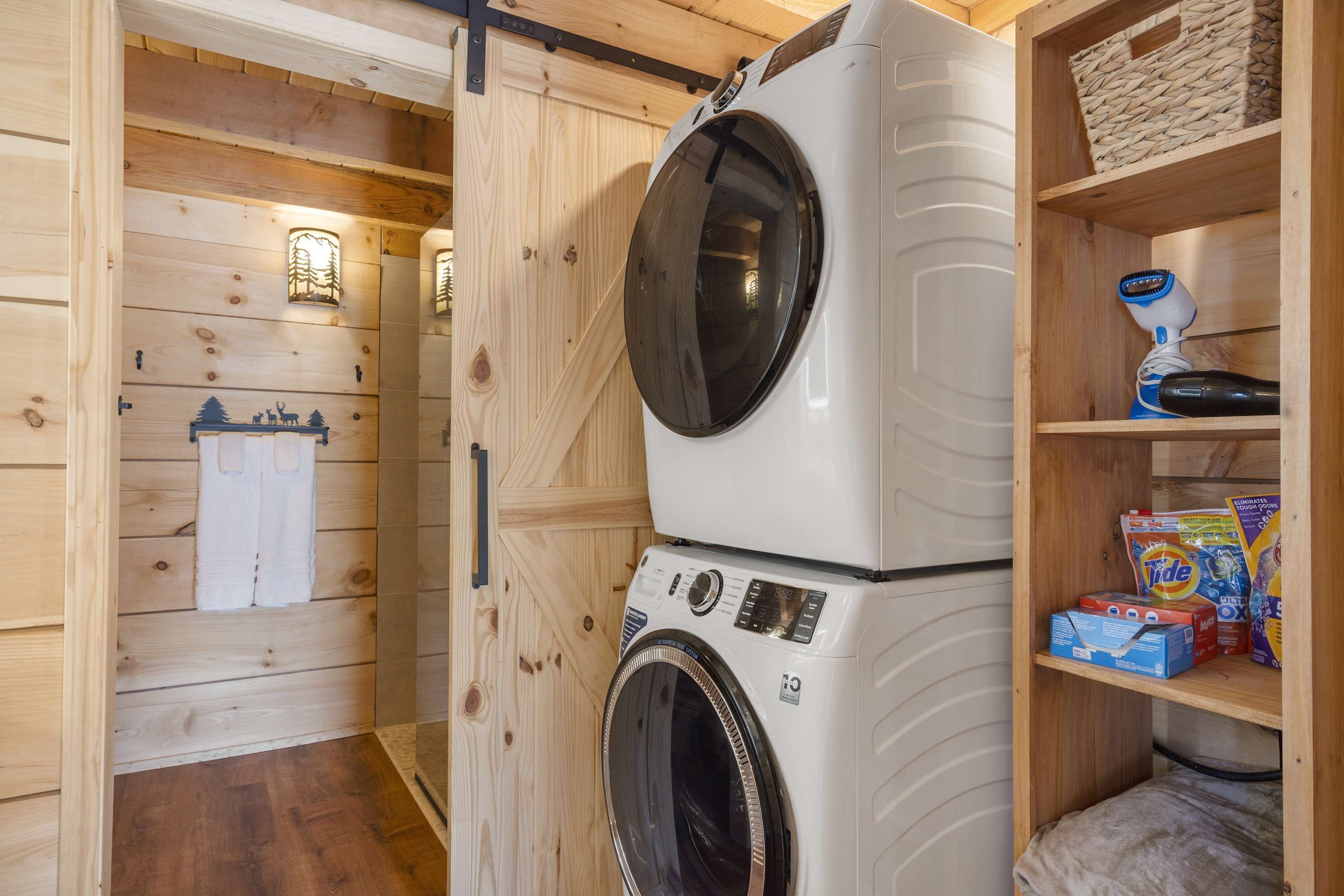 A laundry area with stacked washers and dryers, wooden walls, and shelves with laundry supplies.