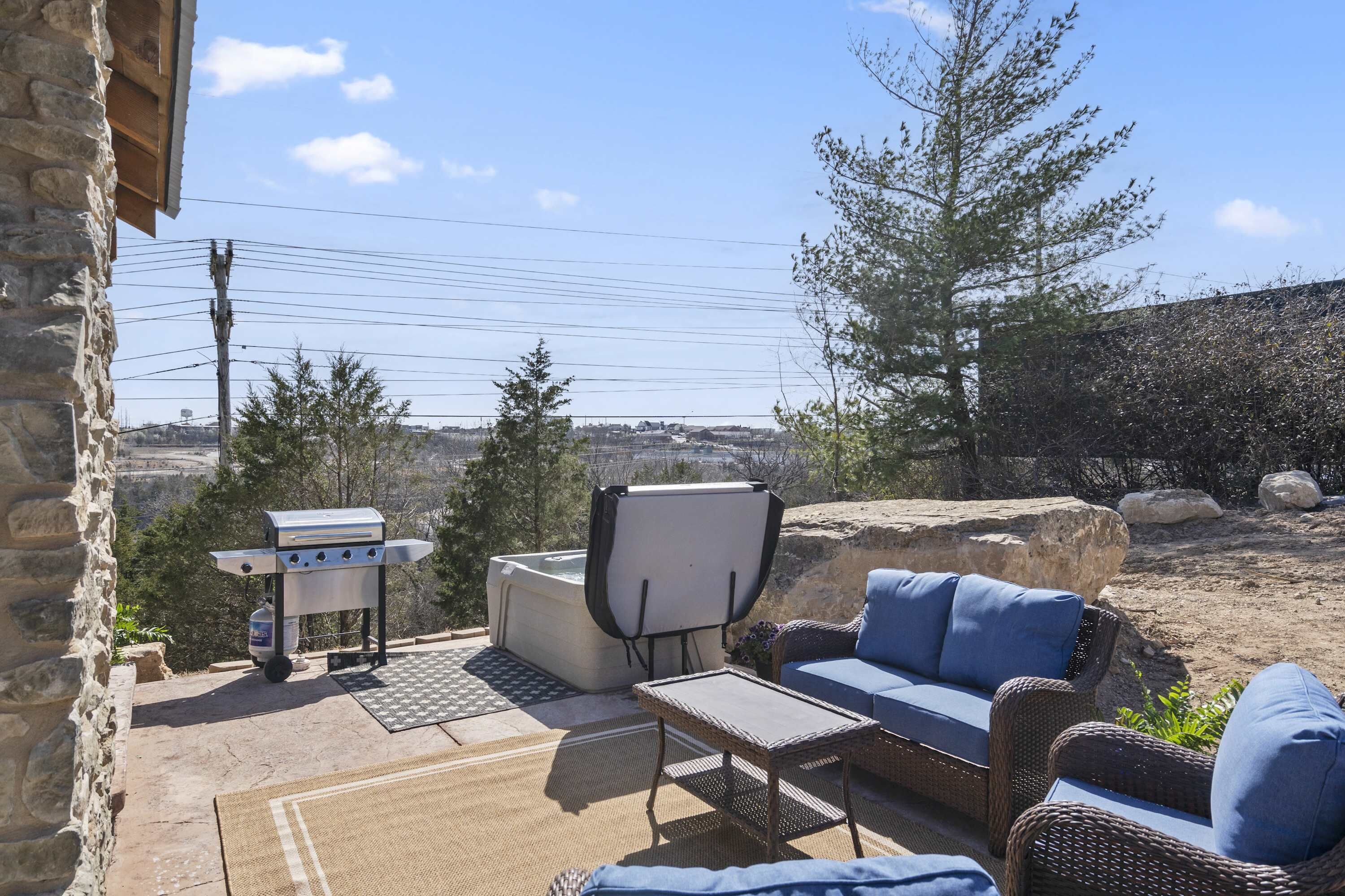 An outdoor patio with a stone wall, a grill, a chair, and a sofa.
