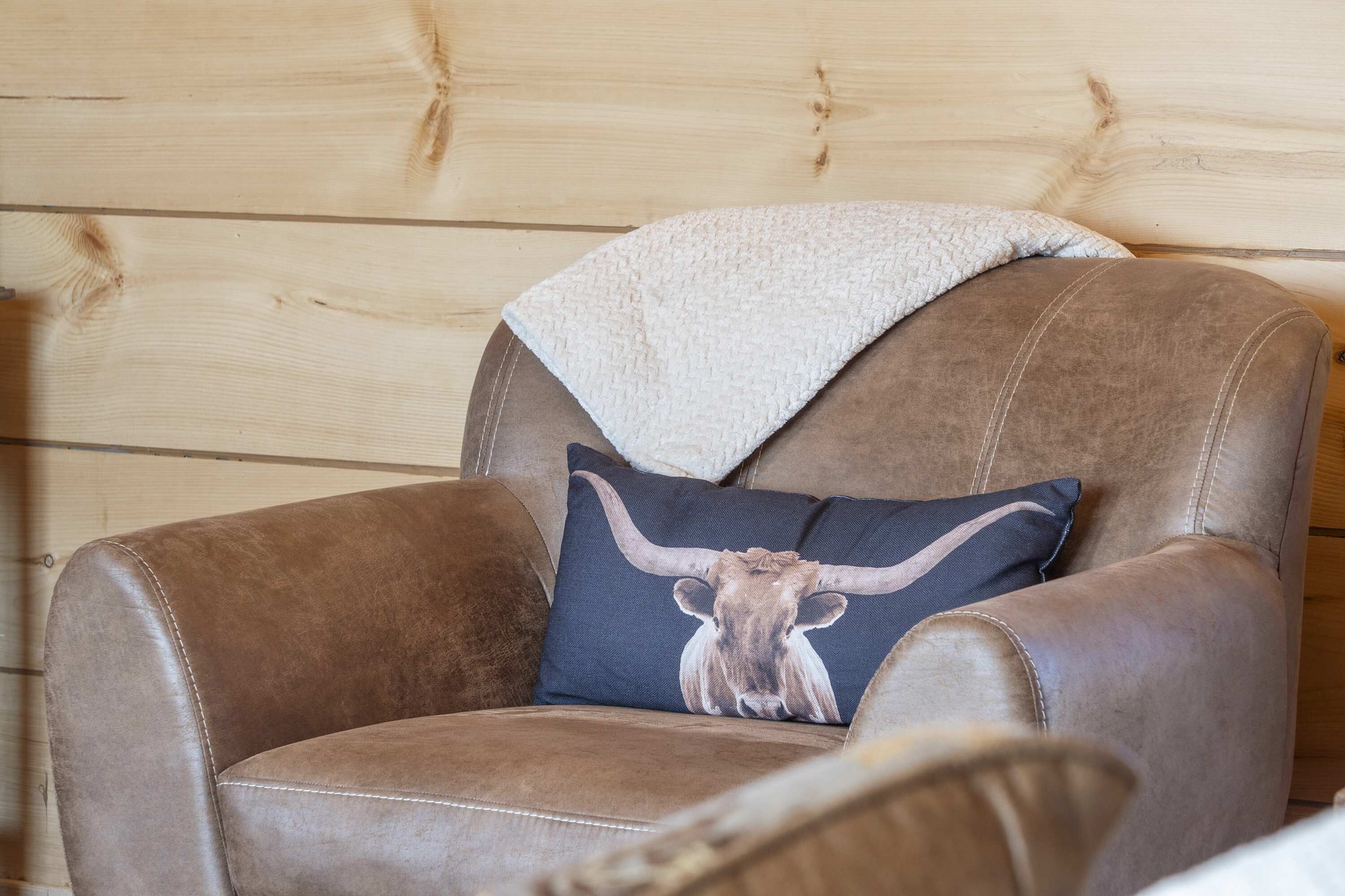 A brown leather armchair with a blanket and a pillow featuring a bull's head design.