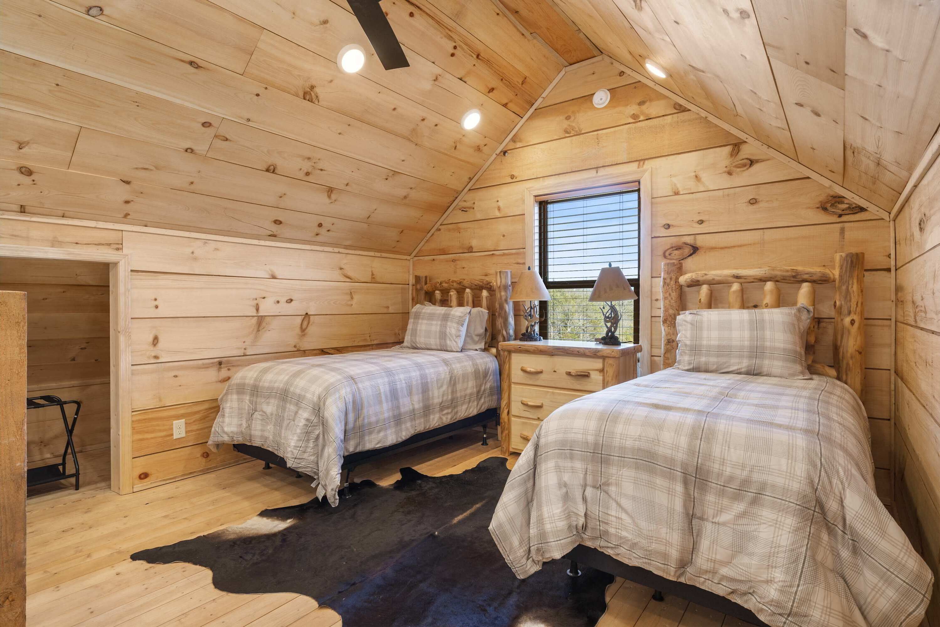 Een slaapkamer in een houten hut met twee bedden, een raam en een kluisvilt vloerkleed.