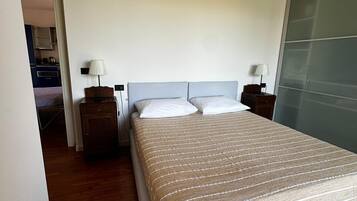 A neatly arranged bedroom with a large bed, two bedside tables, and a view of a kitchen area.