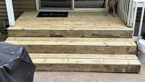 Una terraza de madera que conduce a la entrada de una casa, con un felpudo.
