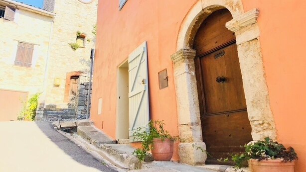 A narrow street with a stone building featuring a wooden door and a clock tower.
