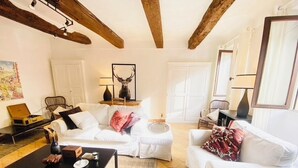 A cozy living room with white sofas, a coffee table, and a fireplace. There are framed pictures on the wall and a lamp on a side table.