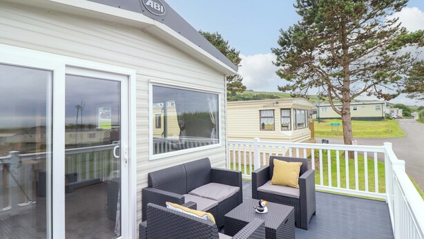 A covered outdoor area with wicker furniture and a glass door leading to a room. - 8 Puffin Way (Llwyngwril)