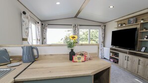 A compact kitchen with a wooden countertop, a built-in TV, and a window with curtains. - 8 Puffin Way (Llwyngwril)
