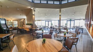 A spacious indoor dining area with multiple round tables and chairs, a wooden ceiling, and large windows allowing natural light. - 8 Puffin Way (Llwyngwril)
