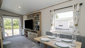 A compact living space with a dining table set for four, a television, and a small kitchenette. - 8 Puffin Way (Llwyngwril)