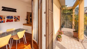A modern apartment with a dining area, a sliding glass door leading to a balcony with potted plants.