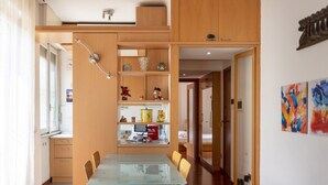 A modern kitchen with wooden cabinets, a glass dining table, and a built-in shelf with various items.