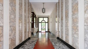 A hallway with a red carpet, marble walls, and a chandelier.