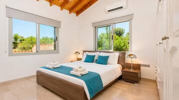 Une chambre avec un plafond en bois, deux fenêtres donnant sur la verdure, un lit avec une literie blanche et bleue, et une table de chevet avec une lampe.