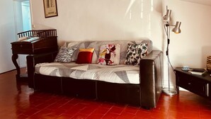 Een woonkamer met een gestreept sofa, een houten bijzettafeltje, een vloerlamp en een lijst met een afbeelding aan de muur.