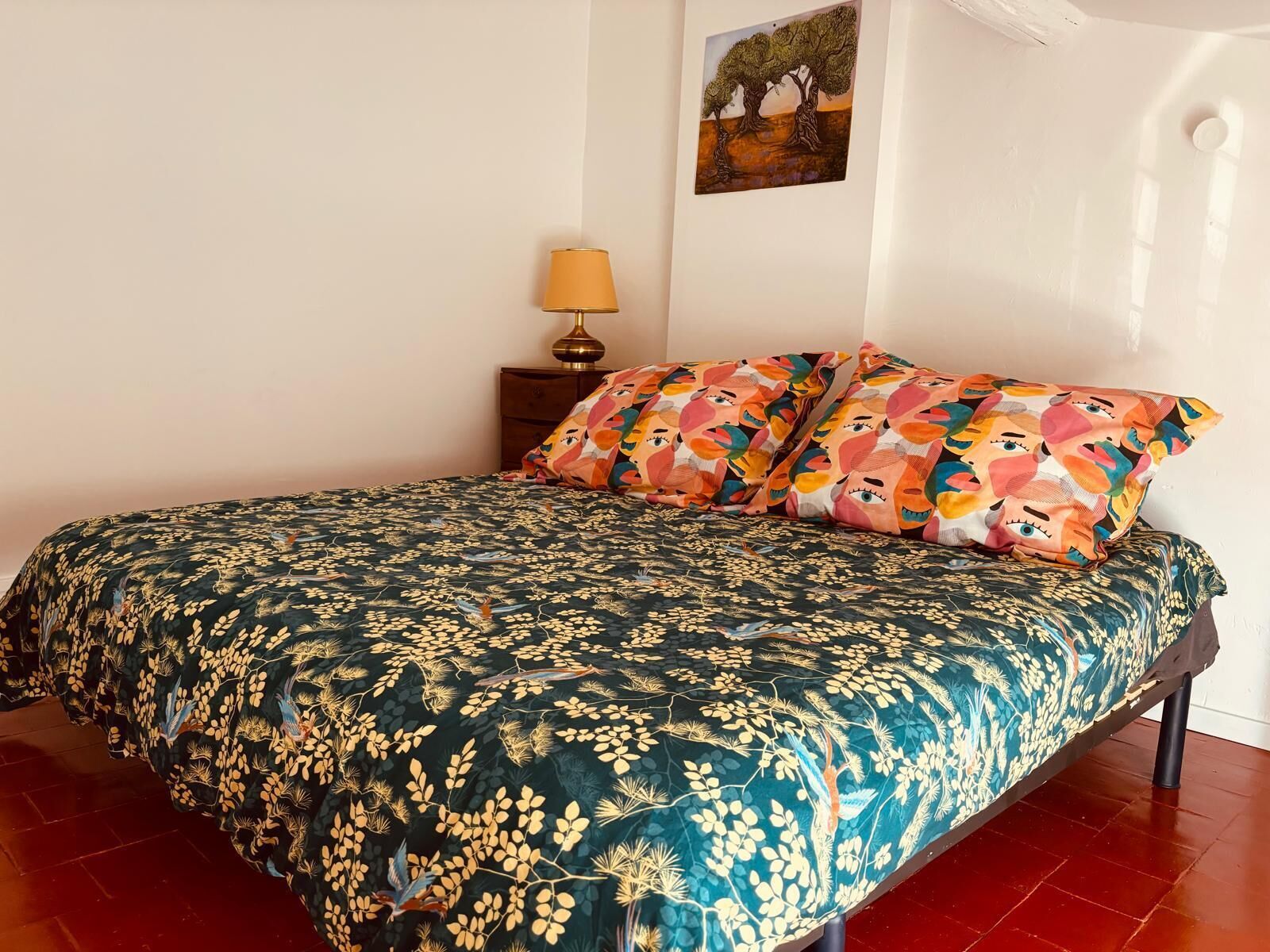 Un dormitorio con una cama, una mesita de noche, una lámpara y un cuadro en la pared.