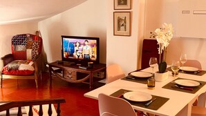 Een gezellige woonkamer met een televisie, een eettafel gedekt voor twee personen en een comfortabele fauteuil.