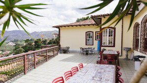 Um terraço com piso de azulejos, uma mesa com cadeiras e vista para uma paisagem montanhosa.