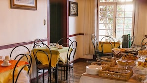 Uma área de refeições com mesas preparadas para o café da manhã, com diversos pães e doces.