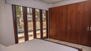 A bedroom with a large bed, wooden wardrobe, and a sliding glass door leading to an outdoor area.